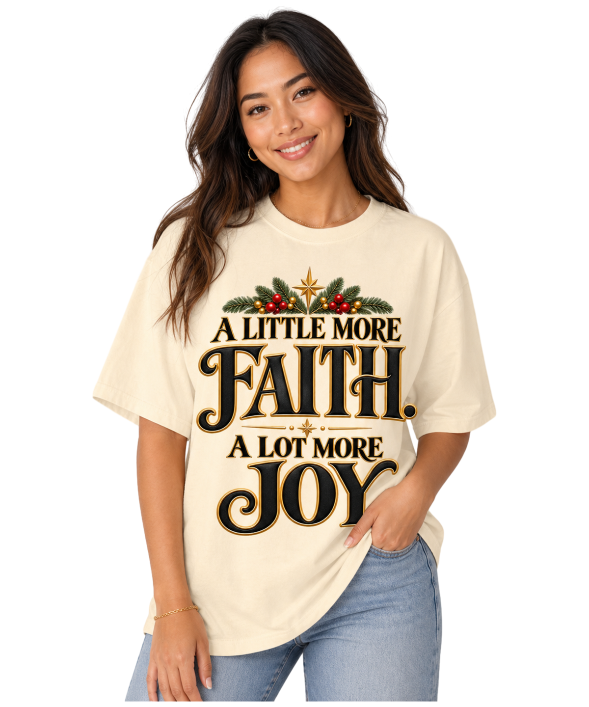 Woman wearing an Ivory “A Little More Faith, A Lot More Joy” Christmas tee with black-and-gold lettering, festive greenery, red berries, and star accents, paired with blue jeans.