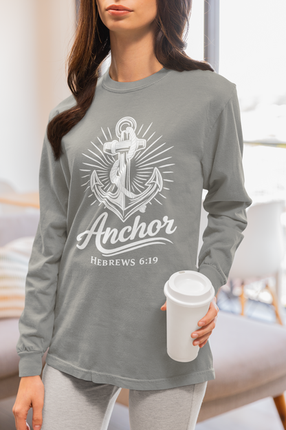 A woman wearing a heather gray long-sleeve t-shirt with a white anchor graphic and the text 'Anchor' and 'HEBREWS 6:19' on the front, holding a white coffee cup in a brightly lit room.