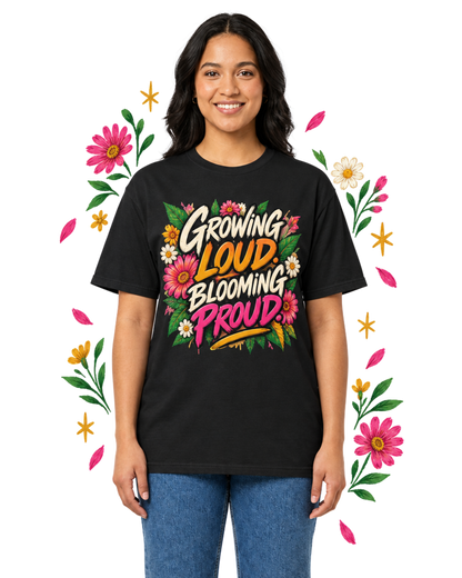 Female model wearing a black Growing Loud, Blooming Proud floral graphic tee with blue jeans, framed by pink, white, and yellow flowers.
