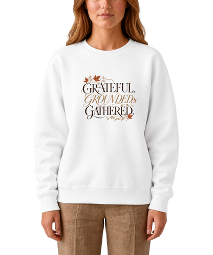 Model wearing a white ‘Grateful. Grounded. Gathered.’ sweatshirt with dark and muted gold lettering and autumn leaf accents.

