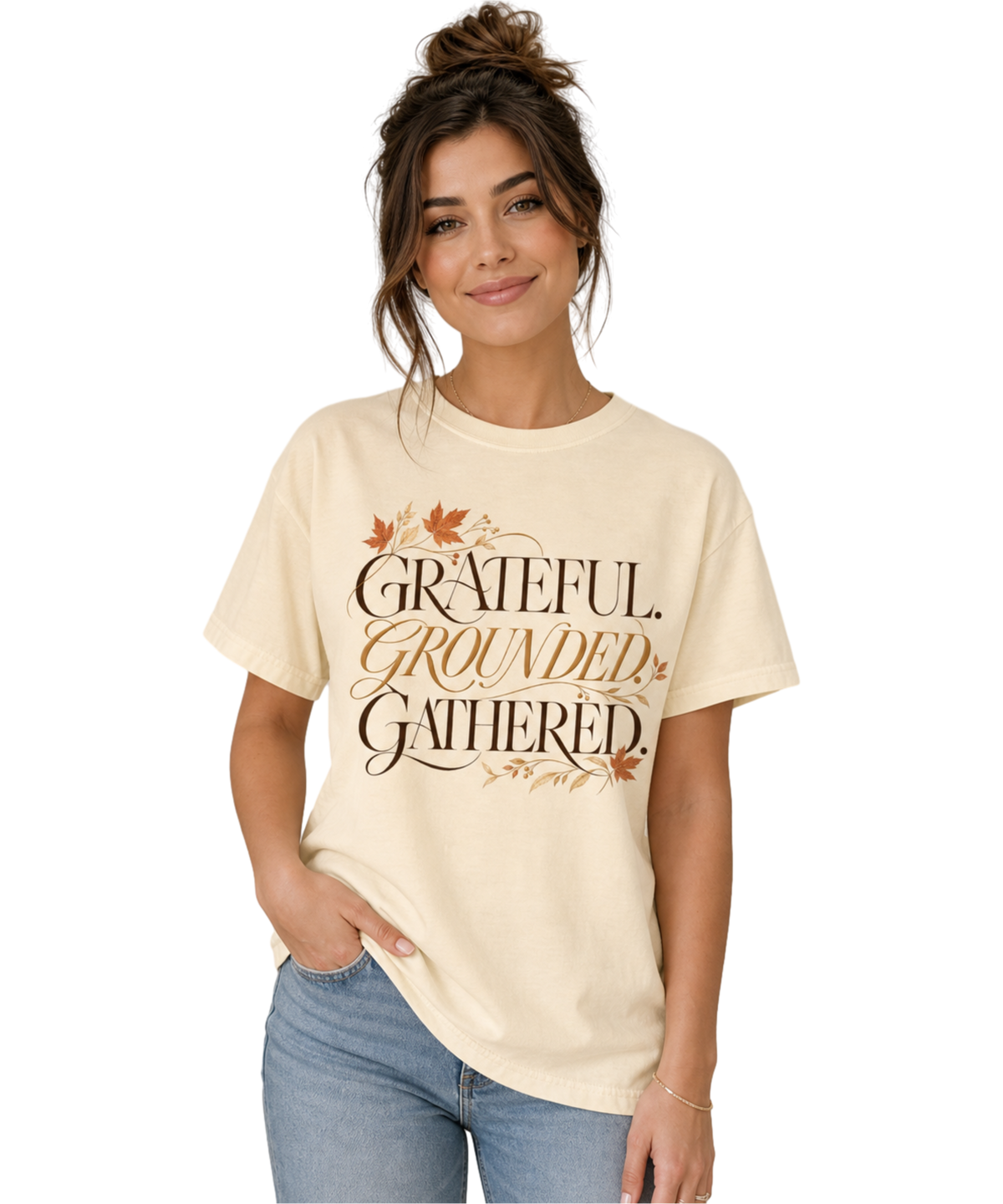 Woman wearing an ivory “Grateful. Grounded. Gathered.” tee featuring autumn leaves and botanical accents, paired with light blue jeans in a softly lit neutral interior.