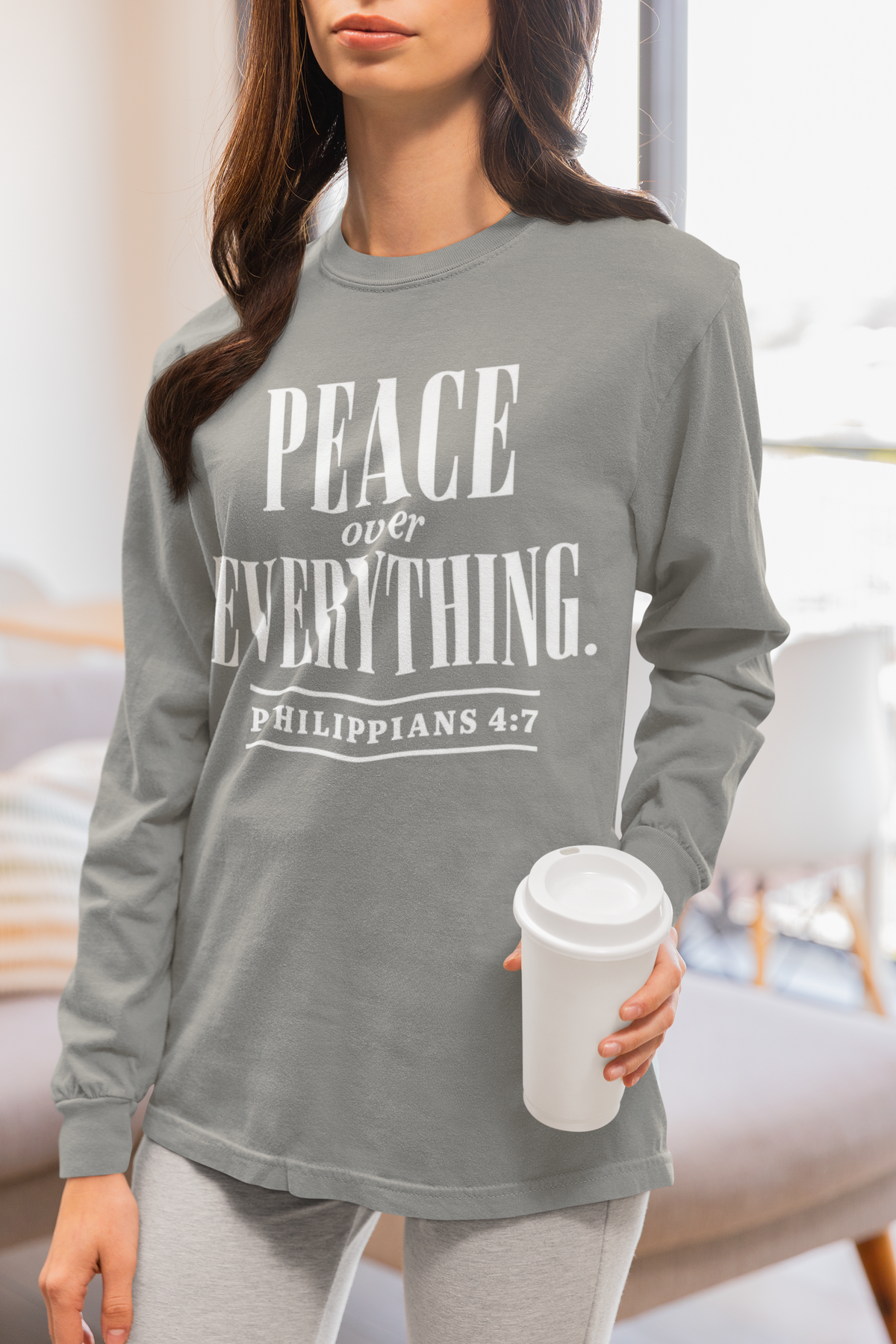 A woman wearing a heather gray long-sleeve t-shirt with a white graphic print that reads 'PEACE over EVERYTHING. PHILIPPIANS 4:7'.