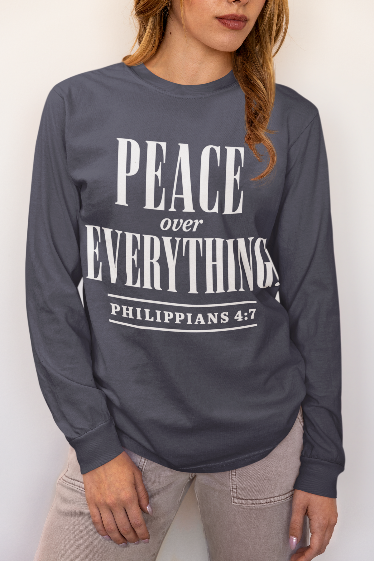 A woman wearing a dark gray long-sleeve t-shirt with a white graphic print that reads 'PEACE over EVERYTHING Philippians 4:7'.