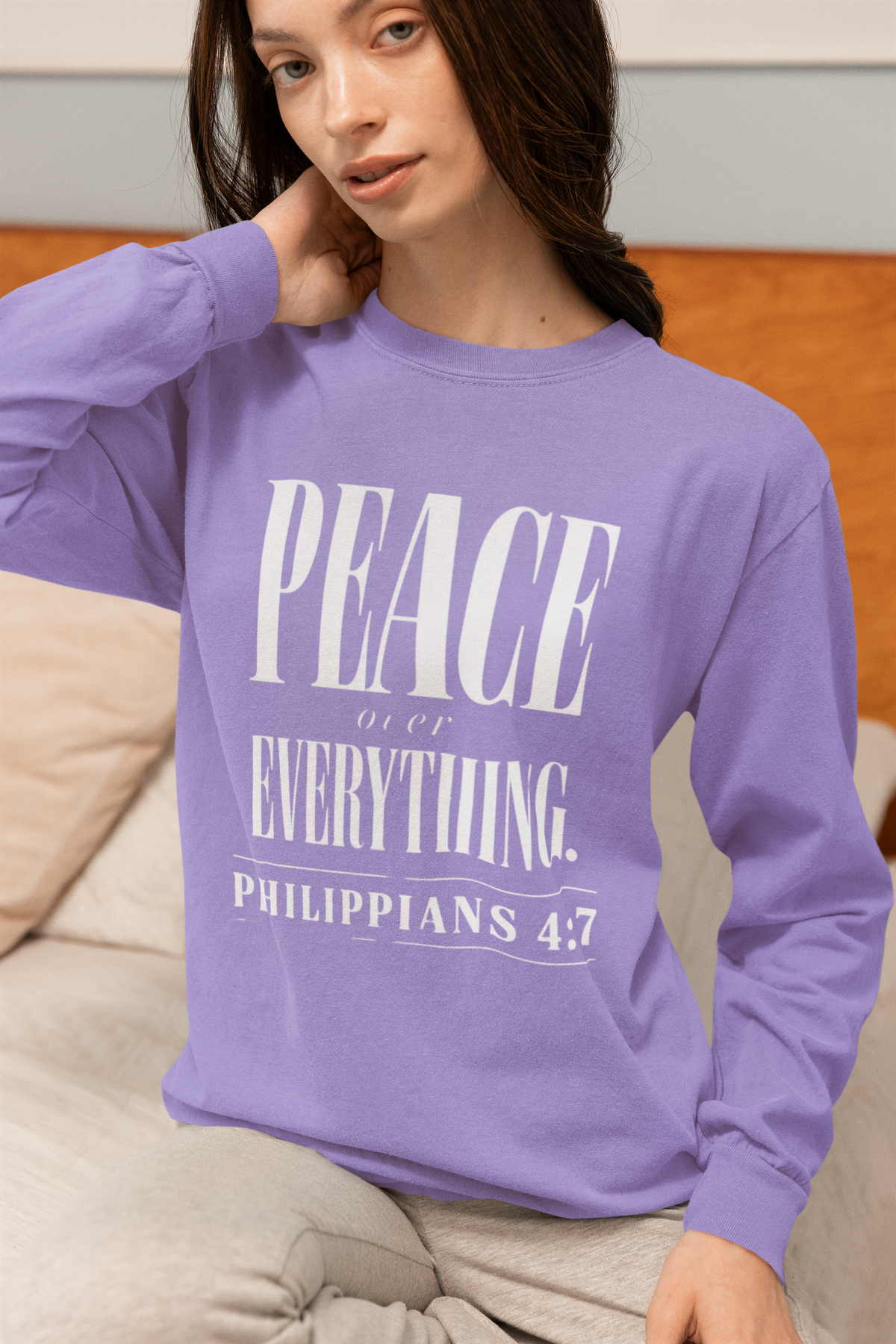 A woman wearing a lavender long-sleeve crewneck sweatshirt with a white graphic print that reads 'PEACE IF NOT EVERYTHING. PHILIPPIANS 4:7'.