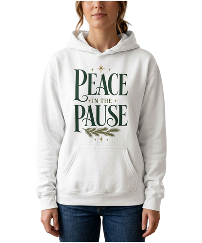 Model wearing a white Peace in the Pause hoodie with forest-green lettering, an evergreen sprig, and gold stars, paired with jeans against a plain white background.