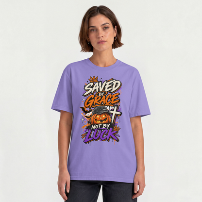 A woman modeling a violet-colored graphic t-shirt with a Halloween-themed design that reads 'SAVED BY GRACE NOT BY LUCK' around a jack-o'-lantern and cross, against a plain off-white background.