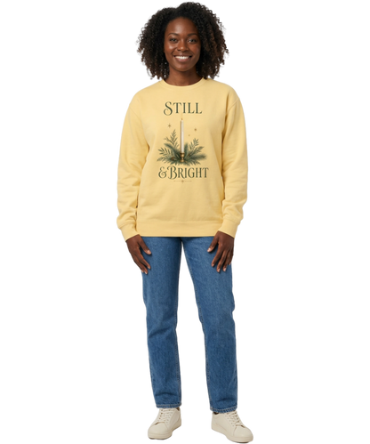 Female model wearing a Butter yellow Still & Bright Christmas sweatshirt with candle and evergreen artwork, blue jeans, and cream sneakers.