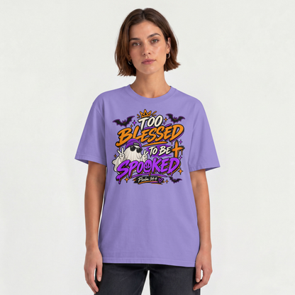 A woman modeling a violet graphic t-shirt Halloween-themed text reading 'Too Blessed to be Spooked' in orange, yellow, and purple, set against a plain off-white background.
