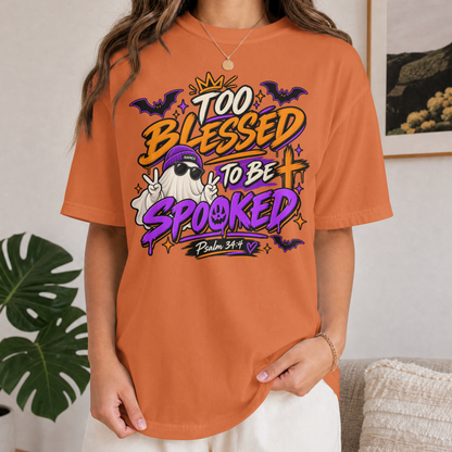 A woman wearing yam-colored graphic t-shirt with a Halloween design that reads 'Too Blessed to Be Spooked Psalm 34:4' featuring a cartoon ghost, bats, and stars.