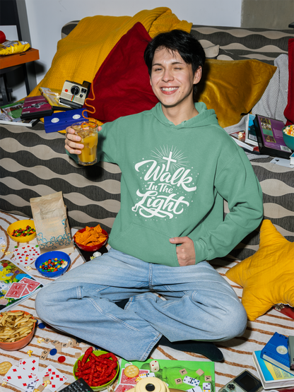 Person wearing a seafoam green hoodie with 'Walk In The Light' text, sitting on a bed with snacks and games.
