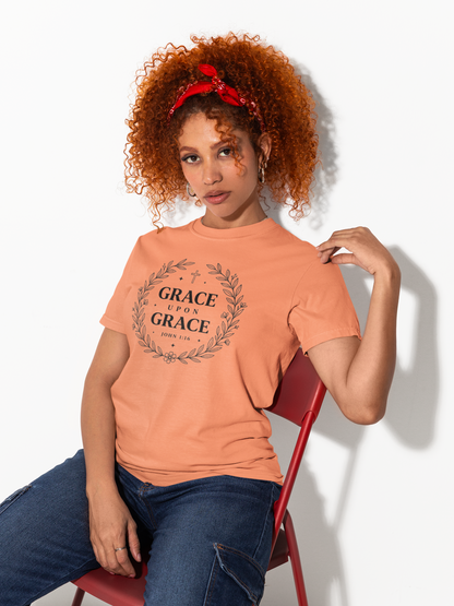 Woman wearing an orange t-shirt with 'Grace Upon Grace' text, sitting on a red chair against a white background.