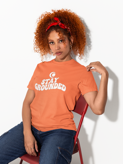 Woman wearing an orange 'Stay Grounded' t-shirt sitting on a red chair.