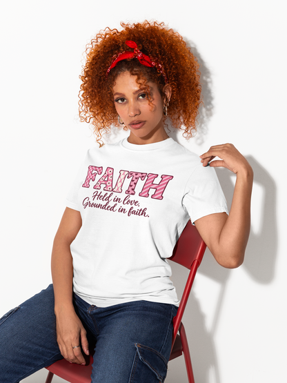 A woman with curly red hair sits on a red chair wearing a white graphic T-shirt with pink text reading 'FAITH Holds in love, Grounded in faith.' and blue jeans against a plain white background.