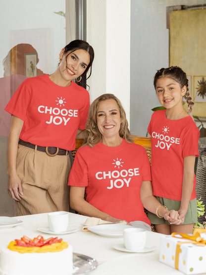 Three people wearing orange 'CHOOSE JOY' t-shirts standing together indoors.