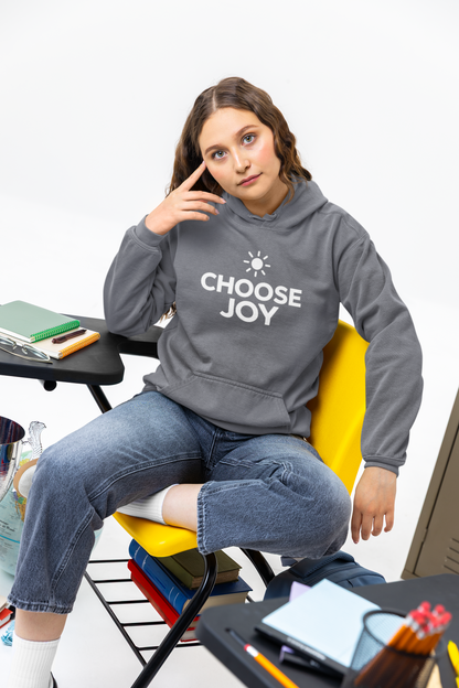 Woman wearing a hoodie with 'CHOOSE JOY' text sitting in a classroom setting.