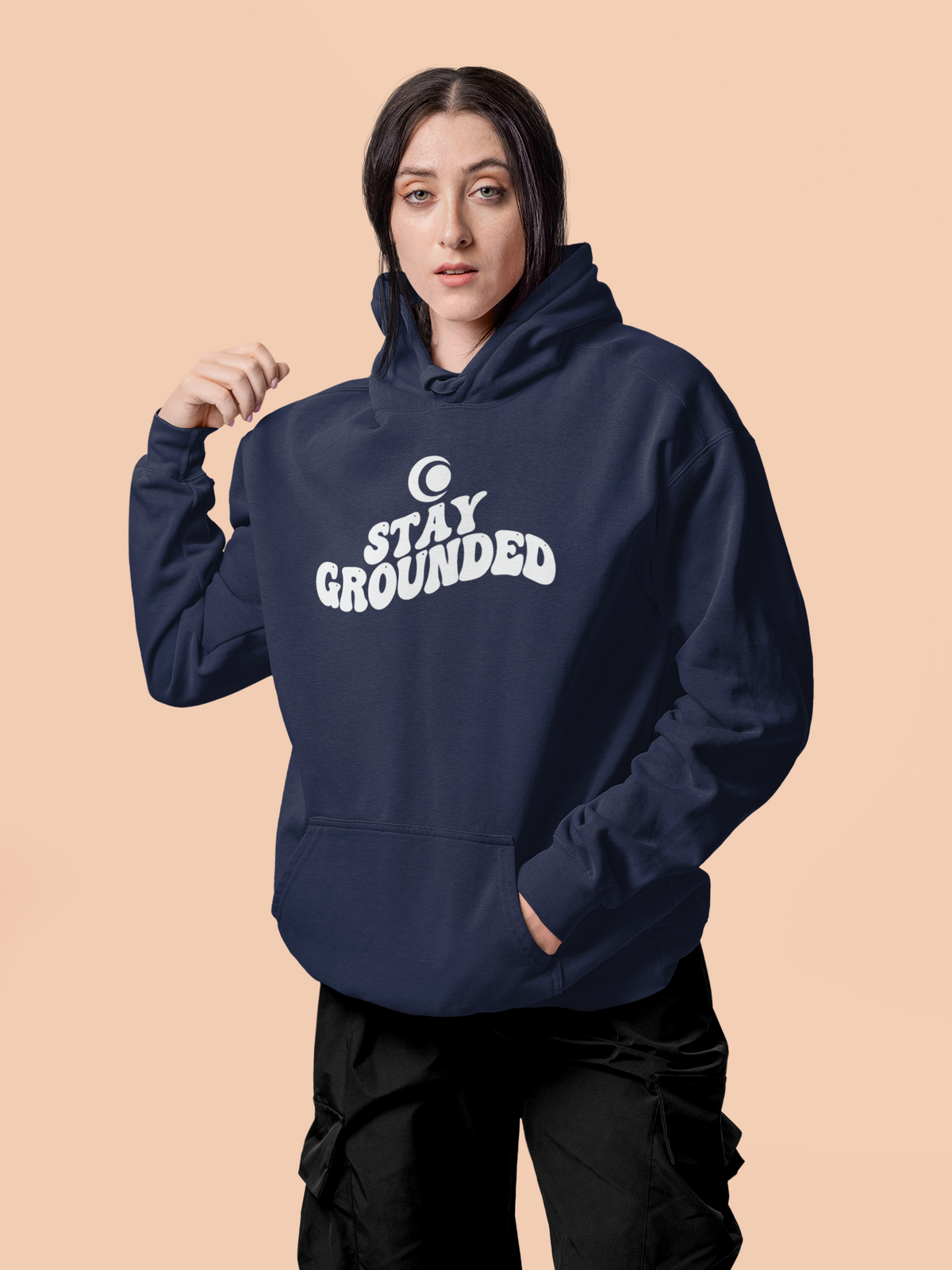 Person wearing a true navy blue hoodie with 'Stay Grounded' text on a beige background