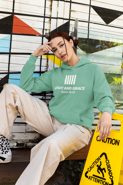 Person wearing a seafoam (green) hoodie with text, sitting on a bench in front of a colorful geometric wall.