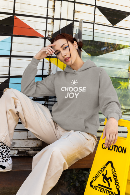 Person wearing a gray hoodie with 'CHOOSE JOY' text, sitting against a colorful geometric wall.