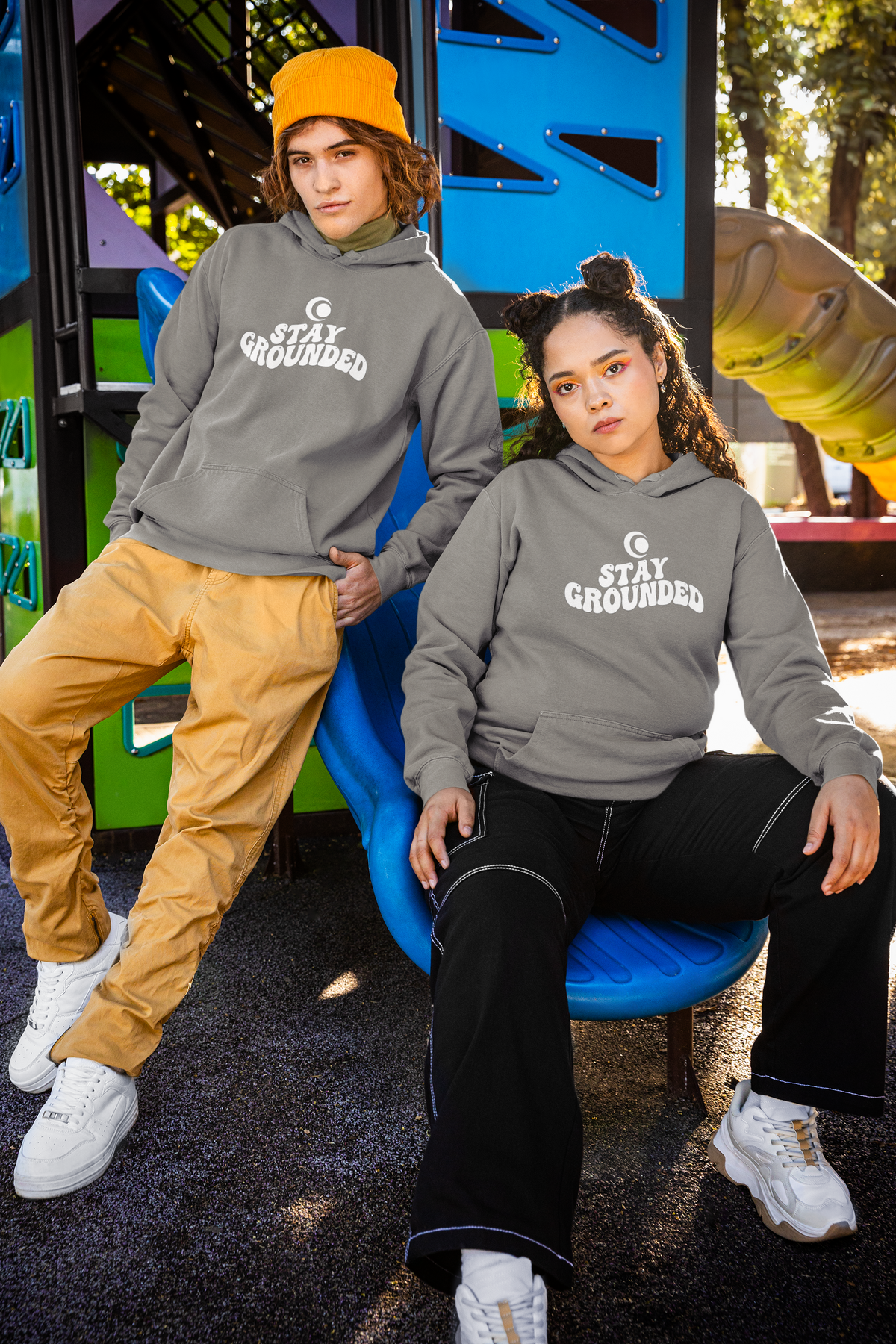 Two people wearing 'Stay Grounded' hoodies in an outdoor setting.
