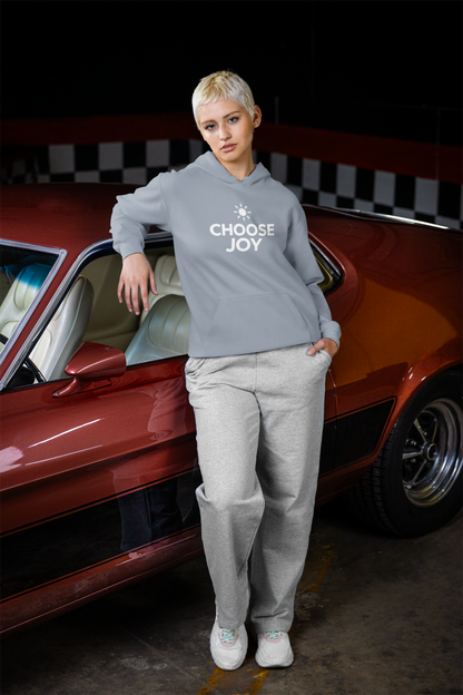 Person wearing a hoodie with 'CHOOSE JOY' text standing next to a red car with a checkered pattern.