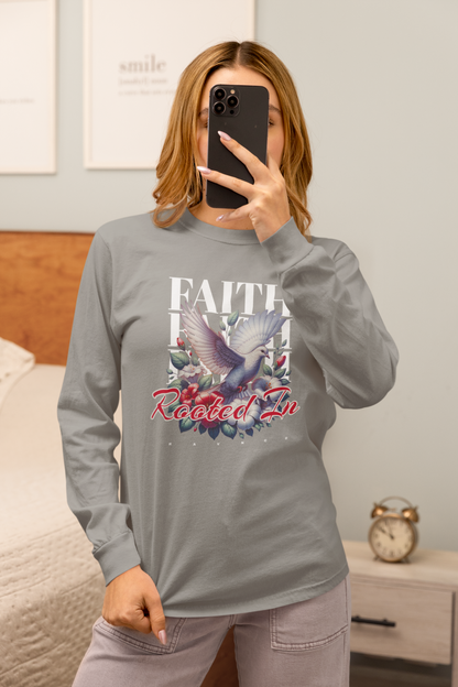 A woman takes a mirror selfie in a bedroom while wearing a gray long-sleeve graphic t-shirt with a dove and floral design, paired with gray pants.