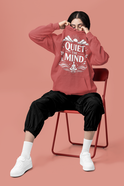 Person wearing a crimson hoodie with 'Quiet the Mind' text, sitting on a red chair against a pink background.