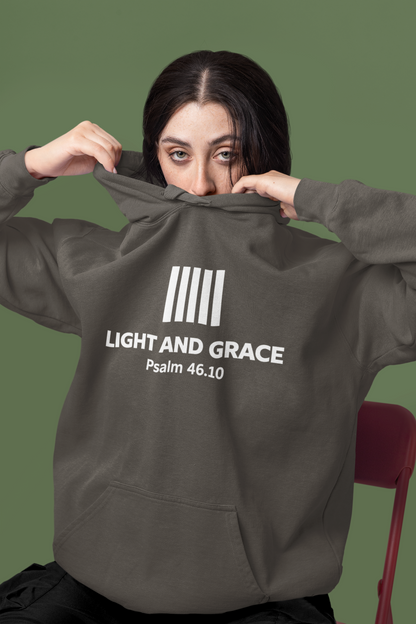 Person wearing a pepper hoodie with 'Light and Grace' text on the back, sitting on a red chair against a green background.