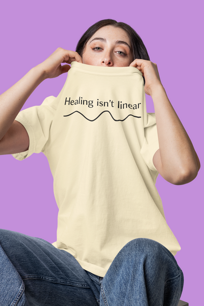 Person wearing an ivory t-shirt with 'Healing isn't linear' text on a purple background