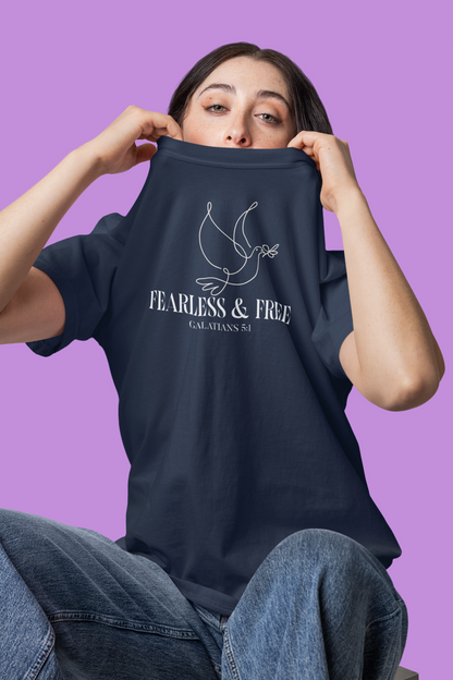Person holding a blue t-shirt with 'Fearless & Free' text and dove graphic on a purple background
