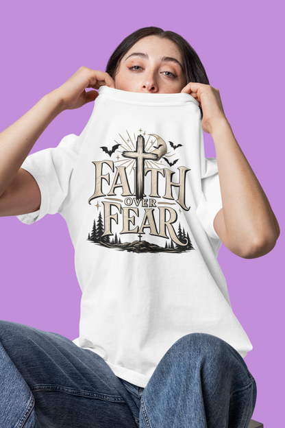 A model wearing a white Comfort Colors garment-dyed t-shirt with the Faith Over Fear Halloween graphic featuring a bold cross, bats, and moonlit forest scene.