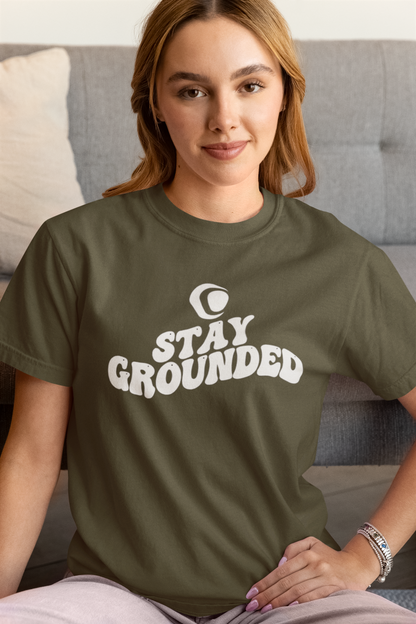 Woman wearing a green t-shirt with 'Stay Grounded' text sitting on a couch.