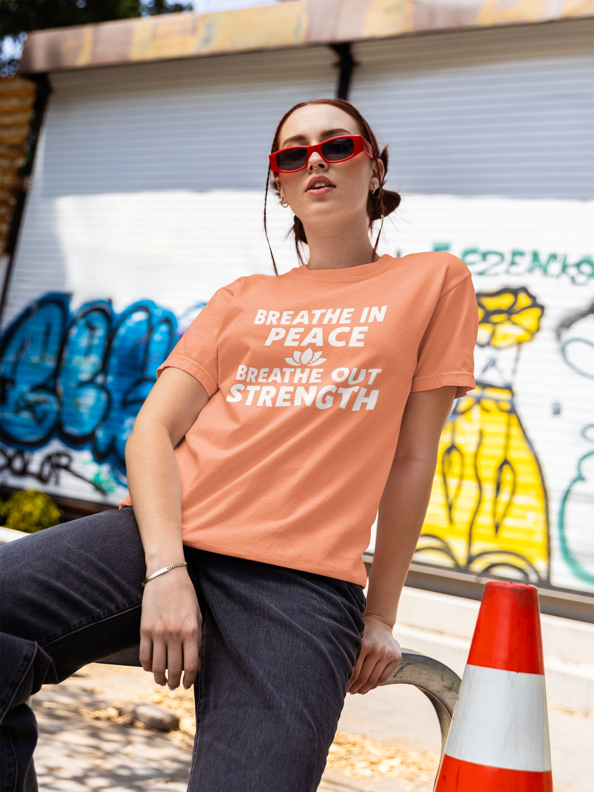 Person wearing a peach t-shirt with motivational text, standing in front of graffiti.