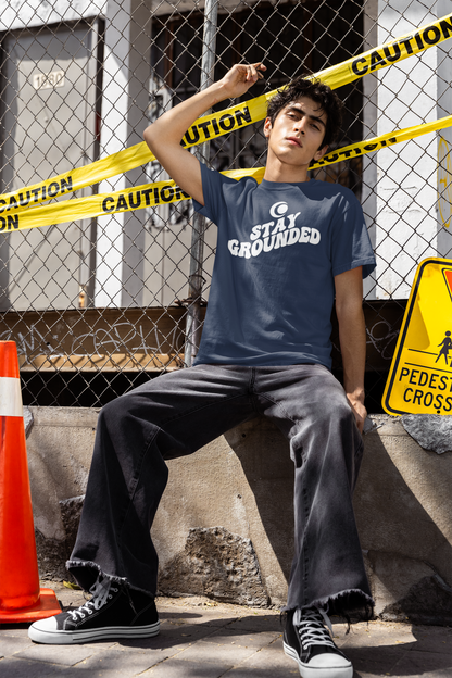 Person wearing a 'Stay Grounded' t-shirt sitting behind caution tape and a pedestrian crossing sign.
