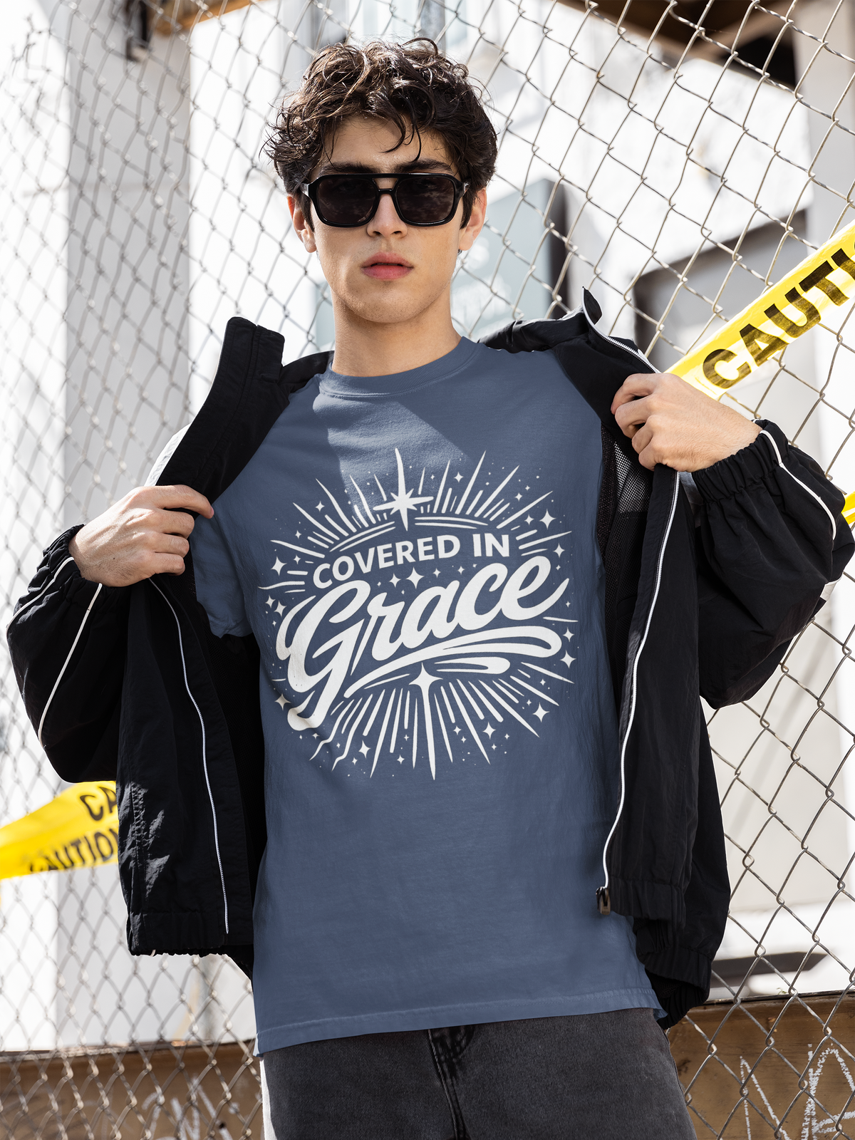 Person wearing a blue t-shirt with 'Covered in Grace' text, standing against a chain-link fence.