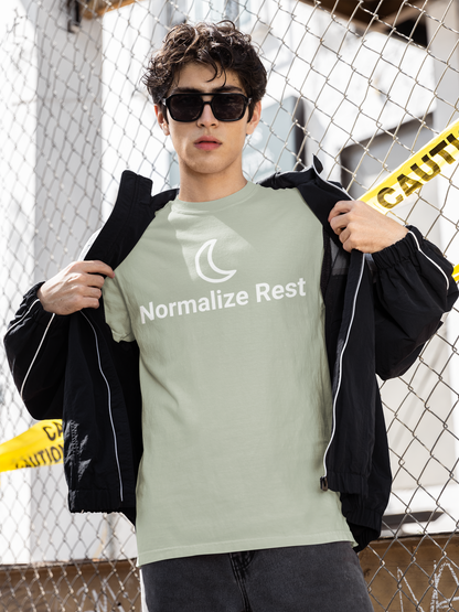 Person wearing a green 'Normalize Rest' t-shirt in front of a chain-link fence.