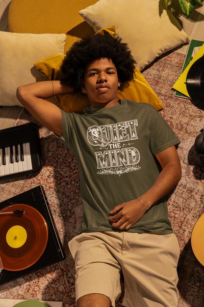 Person wearing a 'Quiet the Mind' t-shirt lying on a patterned rug with musical instruments around