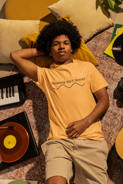 Person wearing a mustard t-shirt with text, lying on a patterned surface with records and a keyboard.