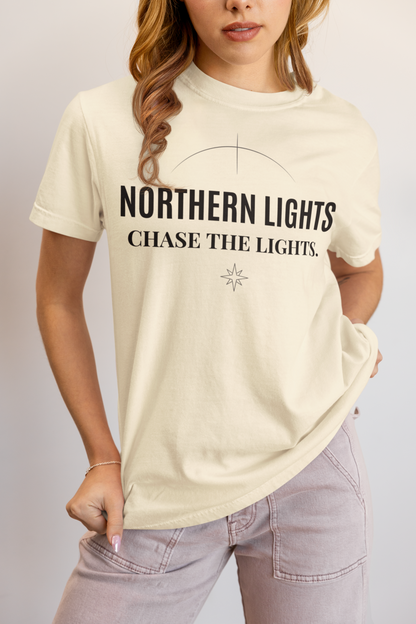 Person wearing an ivory t-shirt with 'Northern Lights Chase the Lights' text on a plain background