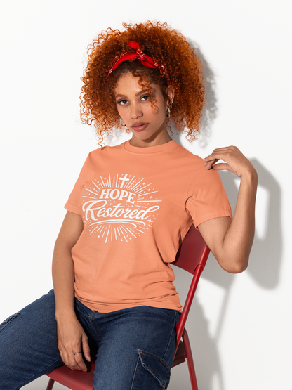 Woman wearing a peach t-shirt with 'Hope Restored' text, sitting on a red chair against a white background.