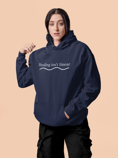 Person wearing a true navy blue hoodie with 'Healing isn't linear' text on a beige background