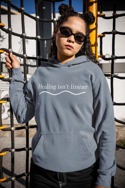 Person wearing a blue jean hoodie with 'Healing isn't linear' text and a moon symbol outdoors.
