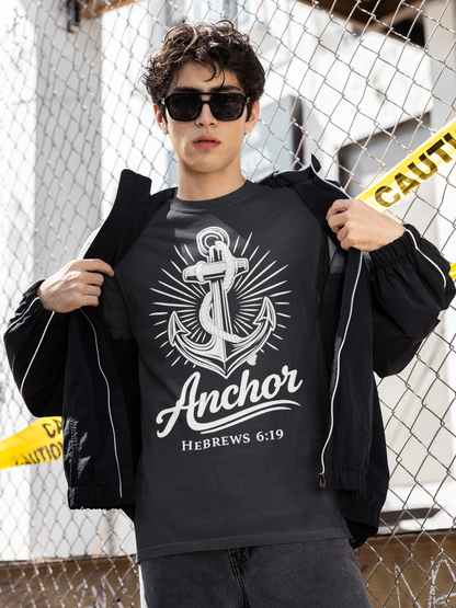 Person wearing a black t-shirt with an anchor design and text, standing against a chain-link fence.