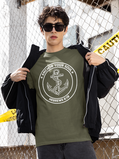 Person wearing a green t-shirt with an anchor design and text, standing against a chain-link fence.