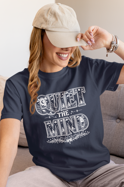 Woman wearing a navy blue t-shirt with 'Quiet the Mind' text, sitting on a couch.