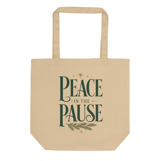 Front view of a natural-colored Peace in the Pause tote bag featuring forest-green lettering, gold stars, and an evergreen sprig.