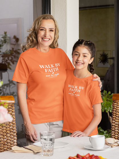 Woman and young girl wearing matching orange t-shirts with 'Walk by Faith not by Sight' text, standing outdoors.
