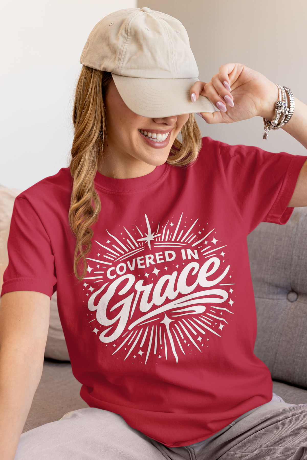 Woman wearing a red t-shirt with 'Covered in Grace' text, sitting on a couch.