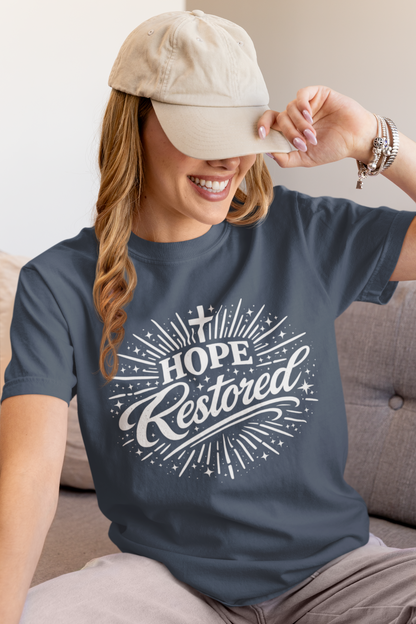 Woman wearing a navy blue t-shirt with 'Hope Restored' text, sitting on a couch.