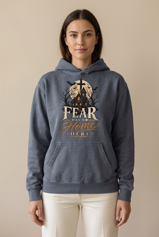 Female model wearing a Denim hoodie with a moonlit house, cross, and ‘Fear Has No Home Here’ lettering, paired with cream trousers.