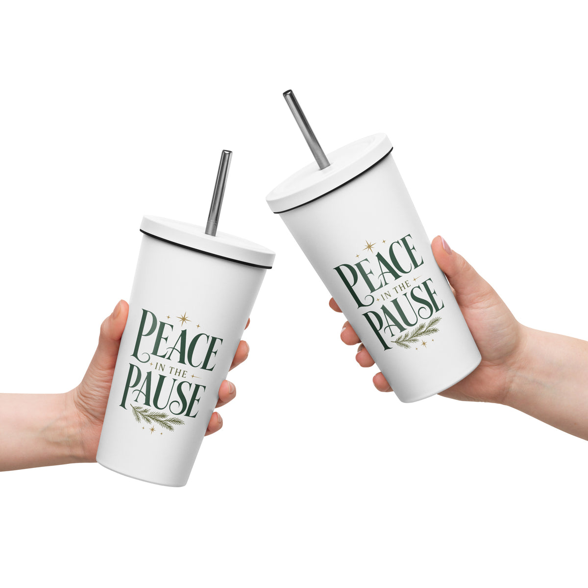 Two hands holding white “Peace in the Pause” tumblers with lids and straws, featuring green lettering and evergreen accents.